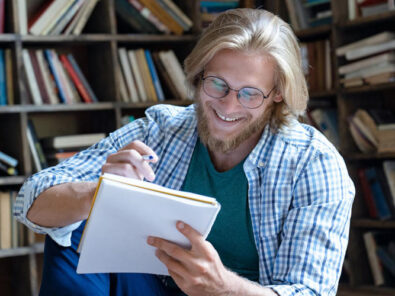 junger Erwachsener sitzt in Bibliothek und lernt etwas Unterhaltsames