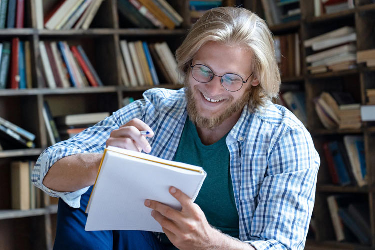 junger Erwachsener sitzt in Bibliothek und lernt etwas Unterhaltsames