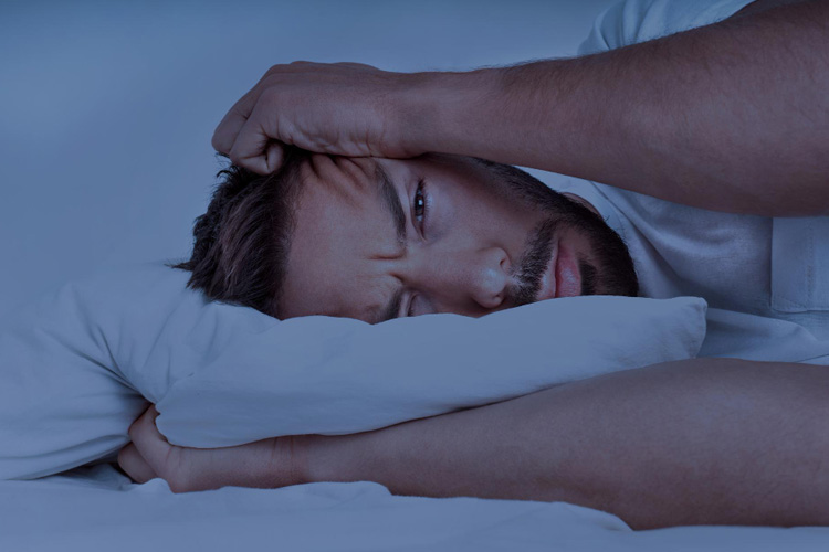 Mann liegt nachts wach im Bett und möchte lieber schlafen