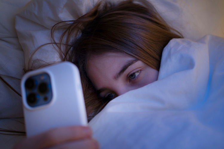 Teenager im Bett mit müden Augen ins Smarphone schauend