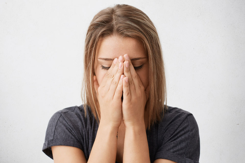 eine Frau versteckt sich vor Peinlichkeit hinter ihren Händen