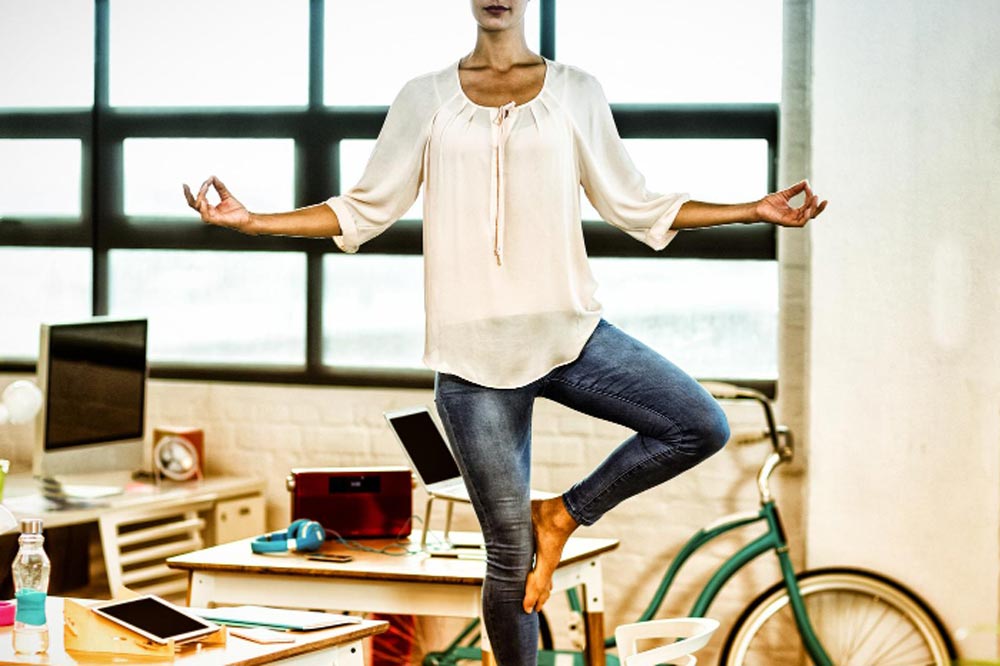 Frau steht in der Tree Pose neben dem Schreibtisch